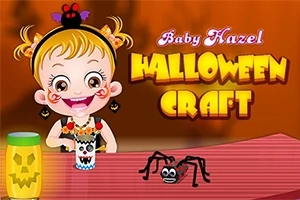 Dieťa s blonďavými vlasmi oblečené v halloweenskej téme, sediace pri stole so strašidelnými dekoráciami a papierovým pavúkom, s nápisom Baby Hazel Halloween Craft