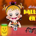 Dieťa s blonďavými vlasmi oblečené v halloweenskej téme, sediace pri stole so strašidelnými dekoráciami a papierovým pavúkom, s nápisom Baby Hazel Halloween Craft