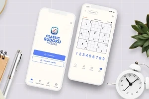 Dva biele smartfóny zobrazujú aplikáciu s úlohou sudoku, obklopené perom, hodinkami a rastlinou