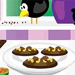 Na obrázku je kuchynská scéna s tanierom čokoládových sušienok ozdobených orechmi, pozadie tvoria rôzne kuchynské pomôcky a vtáčik na parapete