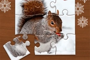 Puzzle s obrázkom veveričky držiacej orech na zasneženom pozadí, s chýbajúcim dielikom v dolnej časti na hnedých stolíku s vločkami
