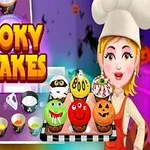 Má farebná postavička kuchárky držiacej tácku s Halloweenskymi koláčikmi a okolo sú rôzne pečené dobroty a nápis Spooky Cupcakes